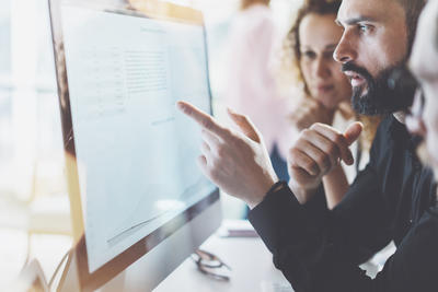 A man pointing out a work issue on his screen to two colleagues