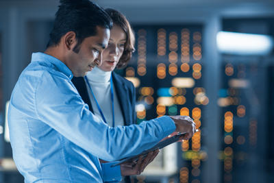 A male and female colleague talk whilst they view a tablet