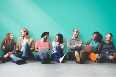 People talking and laughing with laptops against a teal background