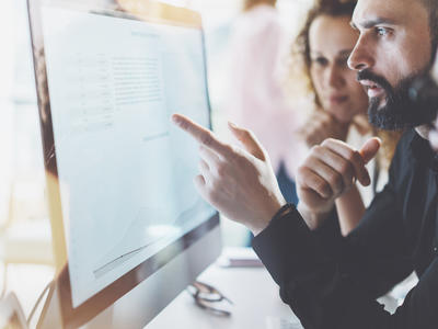 A man pointing out a work issue on his screen to two colleagues