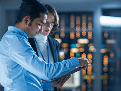 A male and female colleague talk whilst they view a tablet