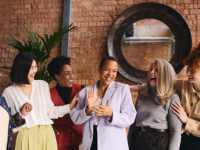 A group of women laughing together in front of a brick wall