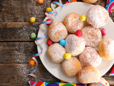 Photo of donoughts on a white plate with a multiple coloured decorations on a wooden table.