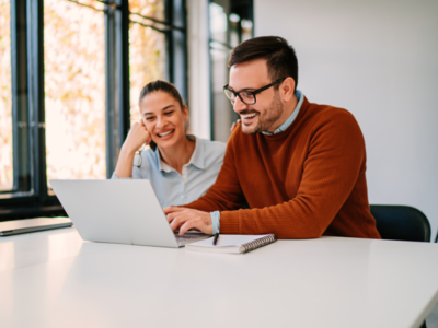 Two people smiling and working on laptop