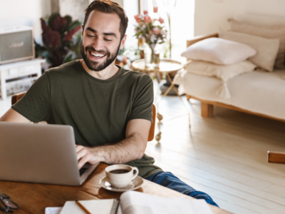 A person smiling while working at a laptop in his living room