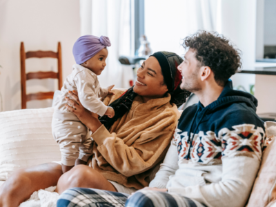 Two people are sitting on a couch with a baby