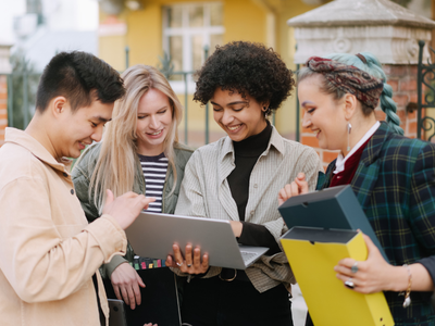 A group of four people gathered around a laptop, looking at the screen and smiling. 